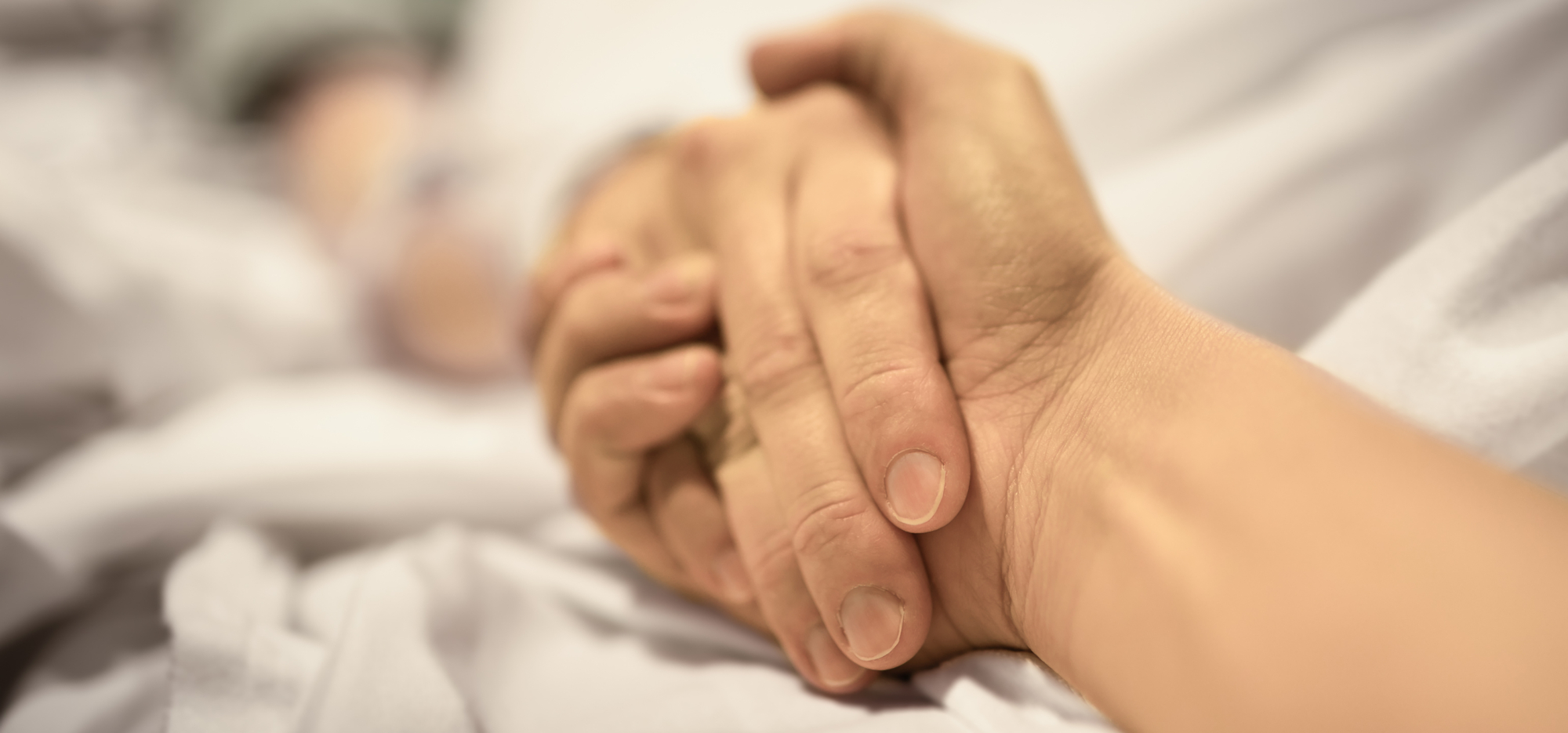 A dying patient and a carer holding hands